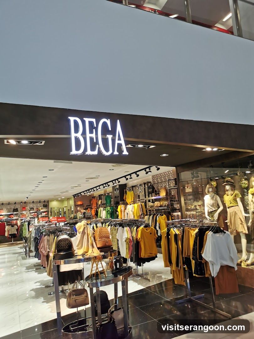 A brightly lit storefront for a clothing store named BEGA, located inside a shopping mall. The store features a wide open entrance with racks of colorful clothing, mannequins in the window display, and a polished floor reflecting the interior lights.