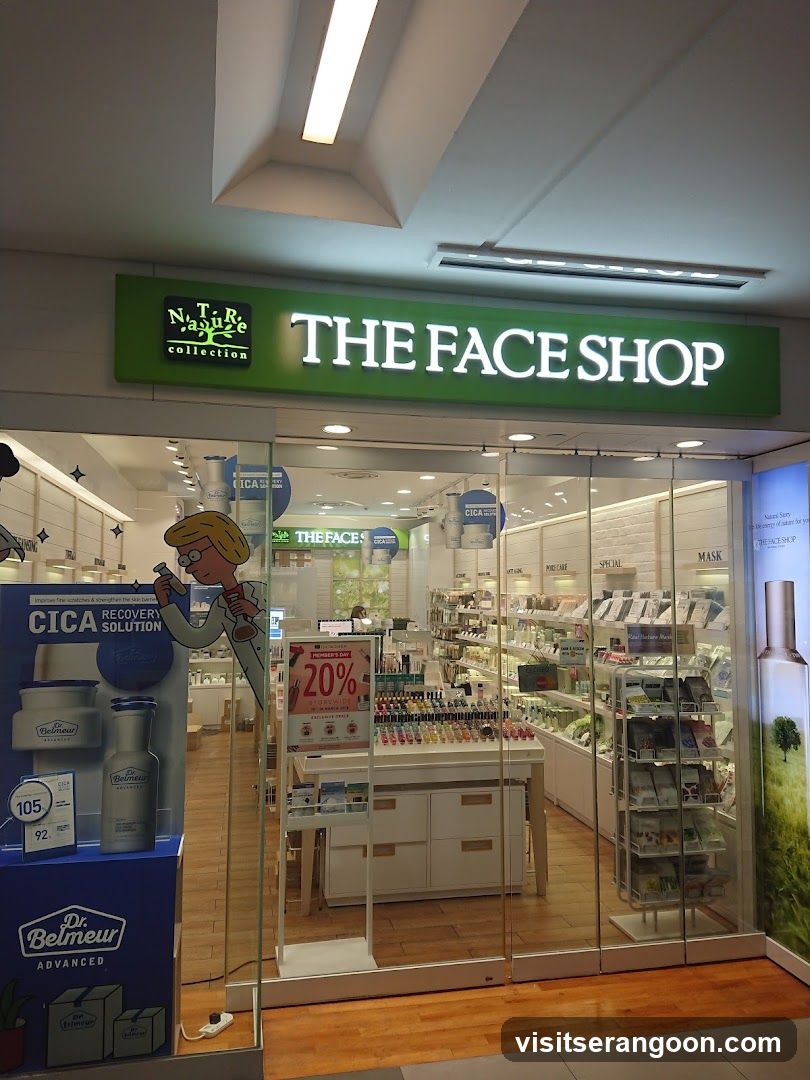 A brightly lit storefront for 'THE FACE SHOP' with a large green sign above the entrance. The store features glass walls and doors, revealing shelves of beauty products inside. A promotional display for 'Dr. Belmeur CICA Recovery Solution' is visible on the left, and a '20% OFF' sale sign stands in the center.