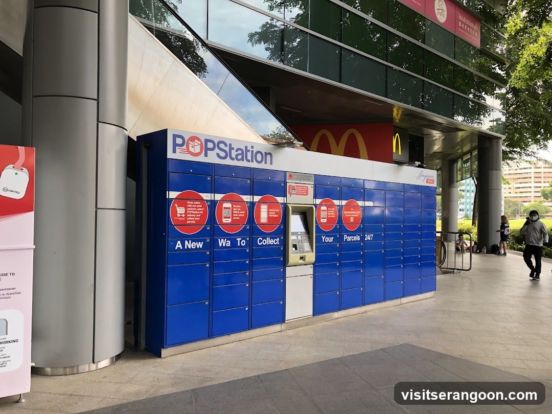 A large blue automated parcel locker unit labeled POPStation is situated on a paved walkway outside a modern building. The unit features a central kiosk and multiple storage compartments. Behind the lockers, a McDonald's sign with its golden arches is visible on the building facade.