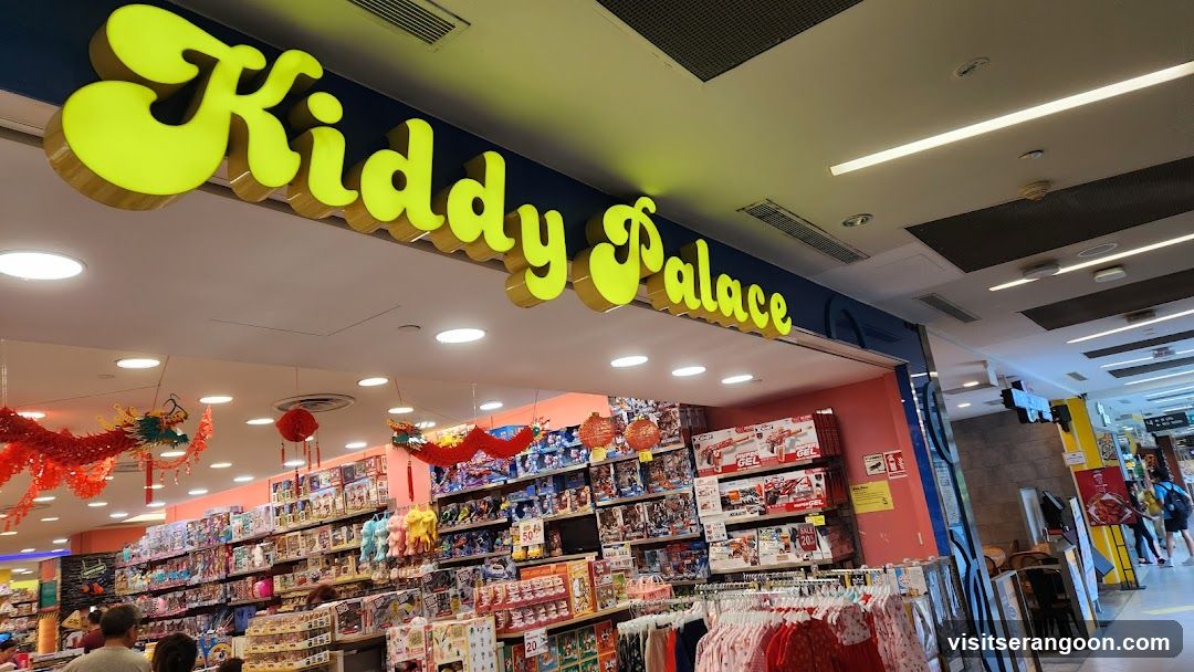 A brightly lit storefront for a store named 'Kiddy Palace' with large, yellow, 3D lettering mounted on a dark blue fascia above the entrance. The interior is visible, showing shelves stocked with toys and hanging red decorations.