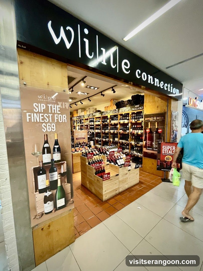 A view of the exterior entrance to a retail store named 'wine connection'. The store features a black sign with white lettering above the entrance. The interior is visible, displaying numerous wine bottles on wooden shelves and in wooden crates. A large promotional poster on the left advertises a wine deal for $69, and a smaller sign on the right advertises 'SUPER STEALS'. A person is walking past the store entrance.