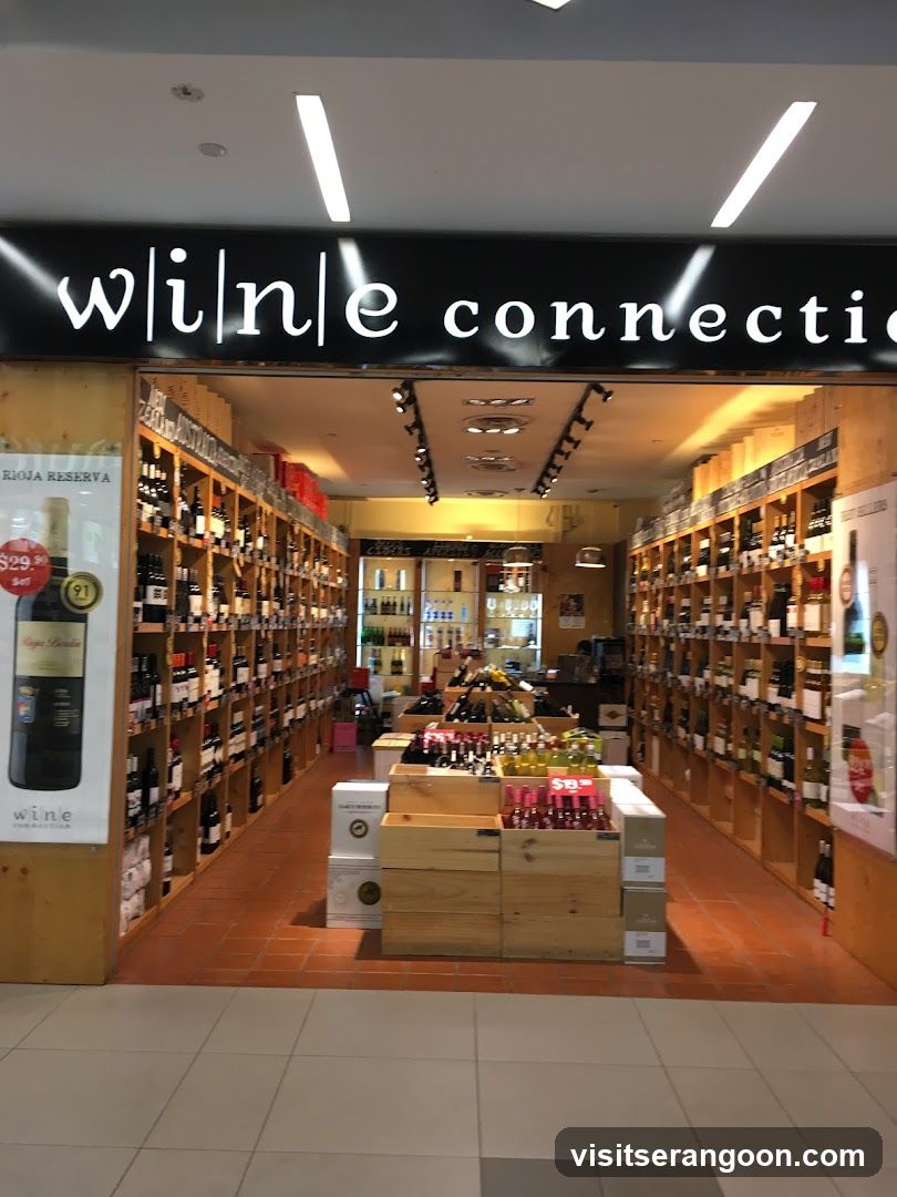 A view of the entrance to a retail store named 'wine connection'. The store has a wide, open entrance with wooden shelving lining the walls, fully stocked with bottles of wine. Inside, there are wooden display crates in the center aisle holding various products. Large promotional posters are visible on the pillars flanking the entrance, advertising specific wine brands and prices.
