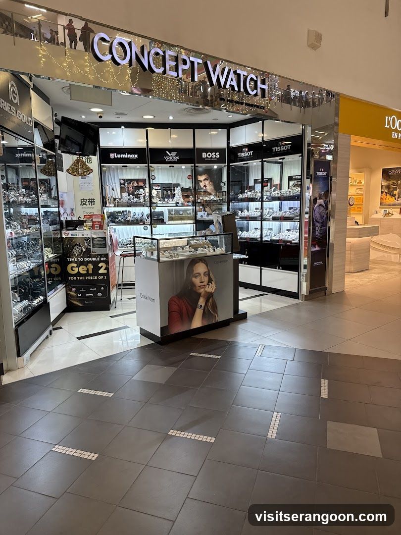 A brightly lit retail store named 'CONCEPT WATCH' located inside a shopping mall. The storefront features glass walls and displays showcasing various watch brands including Luminous, Boss, and Tissot. A large promotional poster of a woman wearing a watch is visible in the center, and a sign advertising a 'Buy 1 Get 2' deal is on the left.
