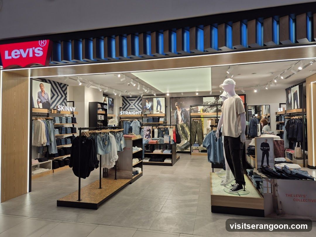 A brightly lit retail store entrance featuring a prominent red Levi's sign with white lettering mounted above the opening. The facade includes a modern design with blue vertical slats and track lighting. Inside, the store displays various denim collections, including 'SKINNY' and 'STRAIGHT' fit signage, alongside mannequins dressed in apparel and racks of clothing.