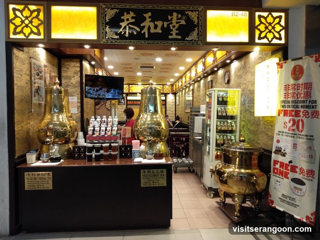 A brightly lit storefront with a prominent black sign featuring gold Chinese characters and the English text 'B2-48'. The entrance is flanked by decorative yellow light boxes. Inside, large golden urns sit on a wooden counter, and a promotional poster advertising a '$20 FREE' deal stands to the right.