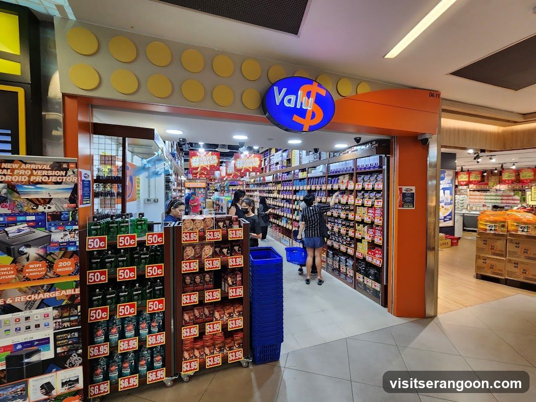 A brightly lit storefront with an orange facade and a blue oval sign reading 'Valu$'. The entrance is open, revealing aisles of merchandise. A promotional display stand is visible on the left, and customers are browsing inside.