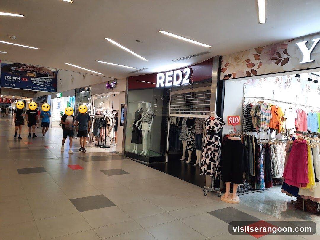 A view of a shopping mall corridor featuring storefronts for RED2 and a clothing store with a large 'Y' sign. Several shoppers with emoji faces are walking past the stores.
