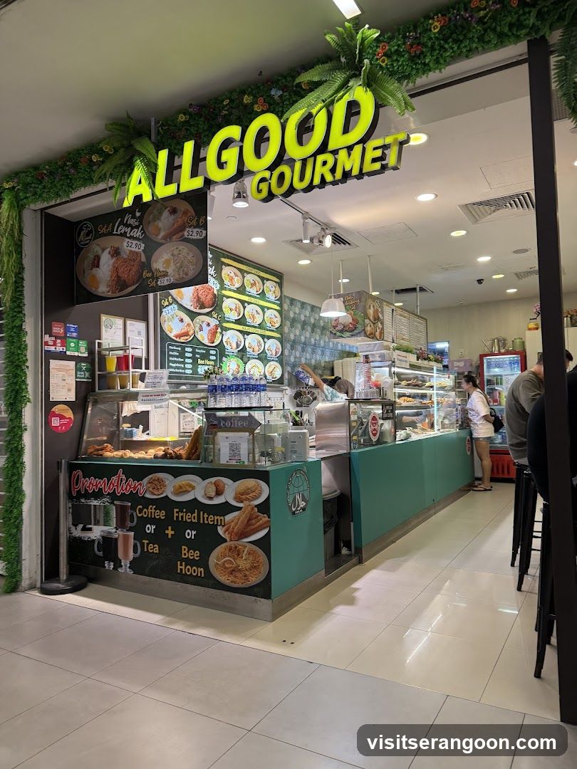 A brightly lit food stall interior with a large neon sign reading 'ALL GOOD GOURMET' in yellow and green letters, surrounded by artificial greenery. The counter is teal, and there are menu boards and promotional posters visible on the walls and counter.