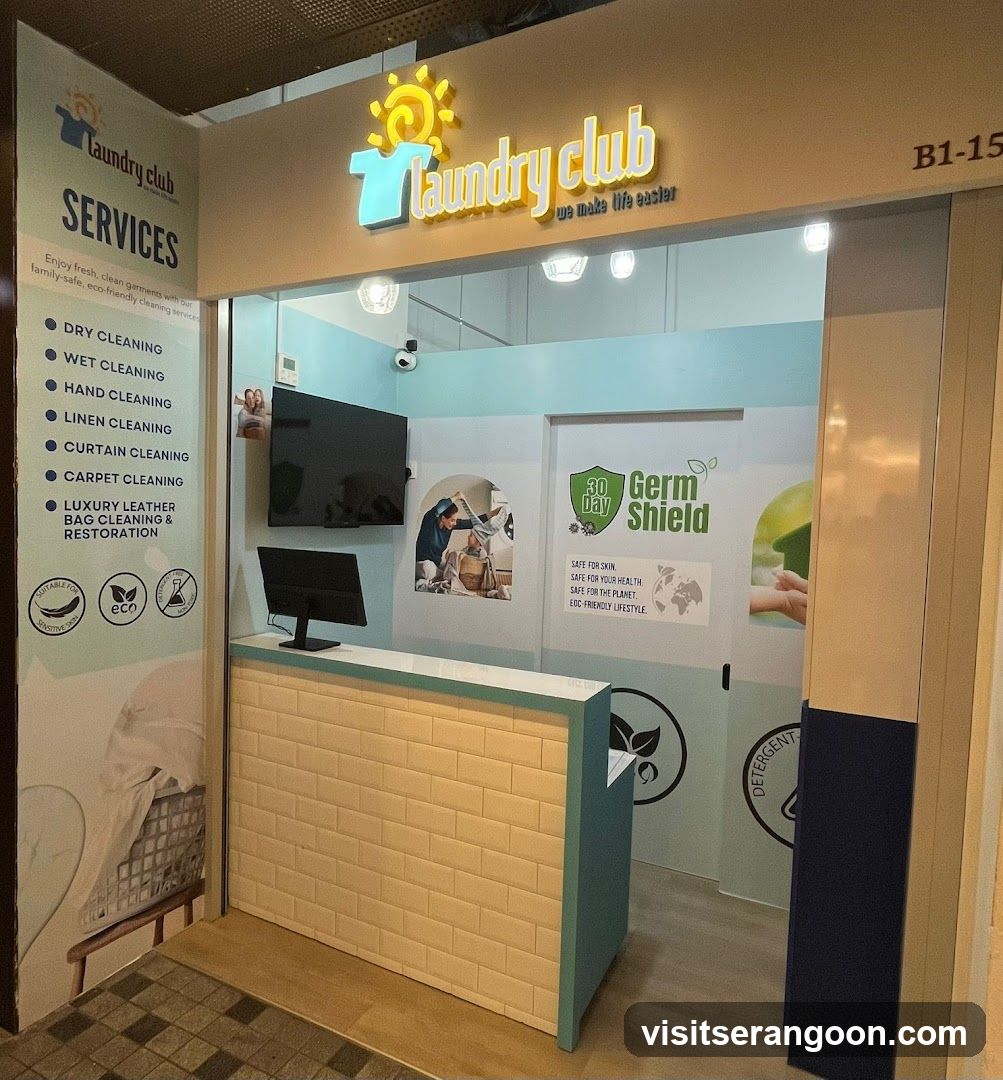A view of the entrance to a laundry service shop named 'Laundry club'. The storefront features a large illuminated sign with a sun logo above the entrance. Inside, there is a reception desk with a computer monitor and a wall-mounted TV. A large vertical banner on the left lists services such as dry cleaning, wet cleaning, and carpet cleaning. The interior walls are light blue and white, with posters advertising 'Germ Shield' and eco-friendly practices.