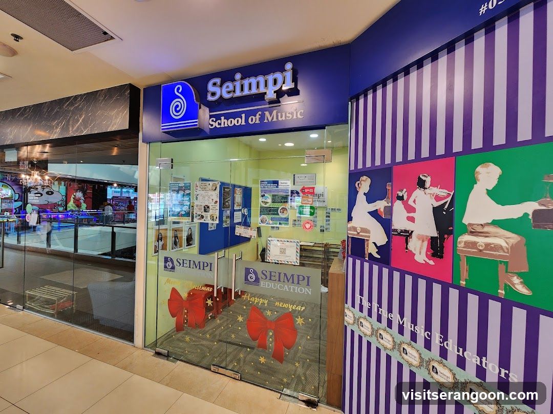 A storefront for Seimpi School of Music located in a shopping mall. The entrance features a blue sign with the business name and logo. The glass doors and windows display posters, flyers, and a 'Happy New Year' graphic. The adjacent wall has purple and white vertical stripes and artwork depicting children playing musical instruments.