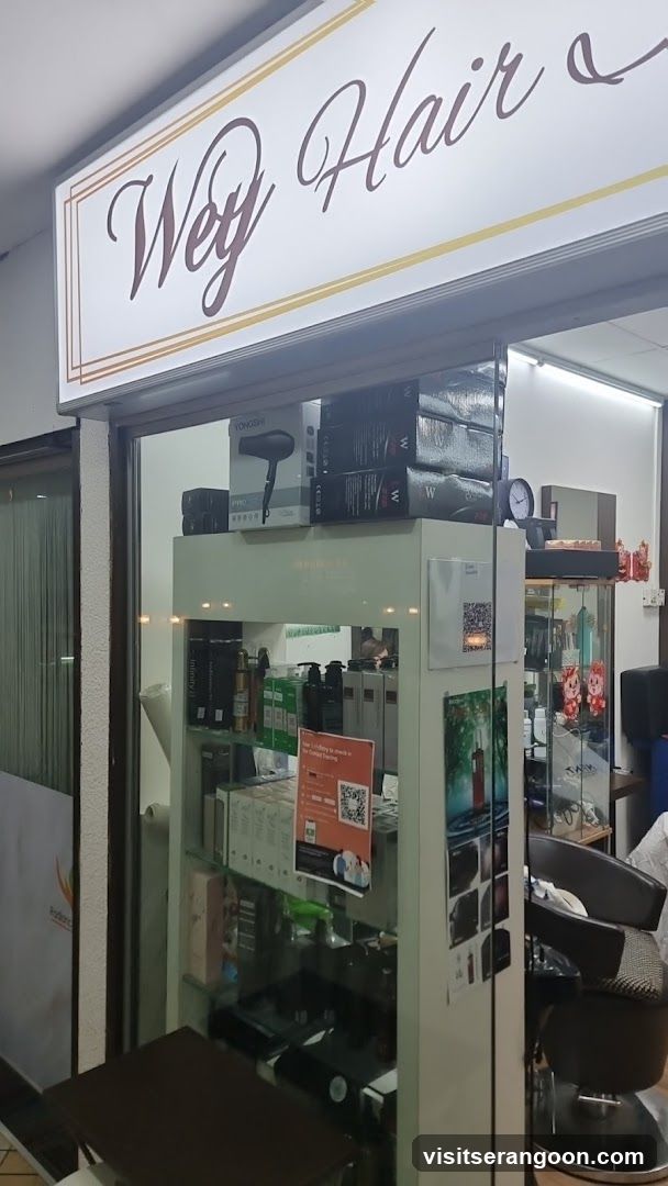 A view of a salon storefront with a large white sign reading 'Wey Hair' in cursive script above the entrance. The glass doors reveal the interior, including a display cabinet stocked with hair products, a black salon chair, and various posters and advertisements on the walls and glass.