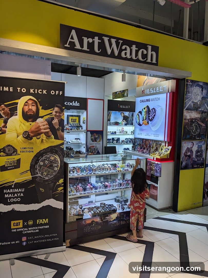 A brightly lit retail store with a yellow facade and a black sign reading 'Art Watch'. The entrance features a glass display case filled with watches, promotional posters for CAT and Kieslect watches, and a child looking at the merchandise.