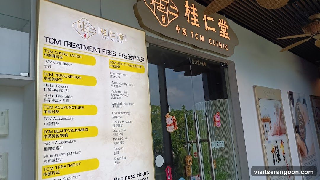 A view of the storefront for a Traditional Chinese Medicine clinic. A large wooden sign above the entrance reads '桂仁堂' and 'TCM CLINIC'. To the left of the glass doors, a large white sign lists 'TCM TREATMENT FEES' and services including consultation, prescription, acupuncture, and beauty treatments. The entrance has glass doors with hanging decorations and a 'OPEN' sign.