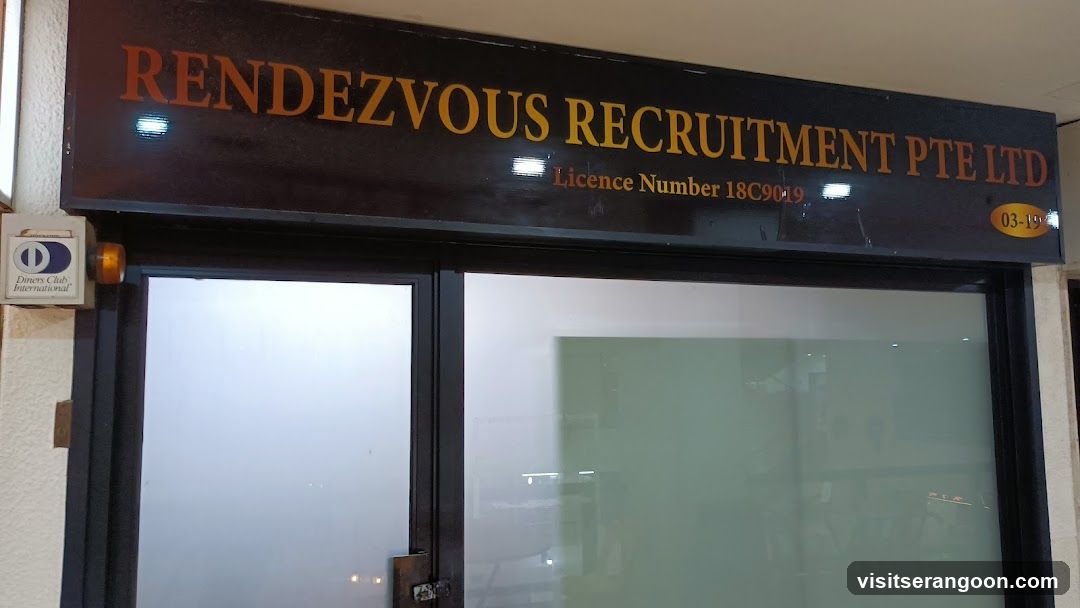 A dark brown storefront sign with gold lettering reading 'RENDEZVOUS RECRUITMENT PTE LTD'. Below the main text, smaller text displays 'Licence Number 18C9019'. The sign is mounted above glass doors with frosted lower panels and black frames. A small security device is visible on the wall to the left.