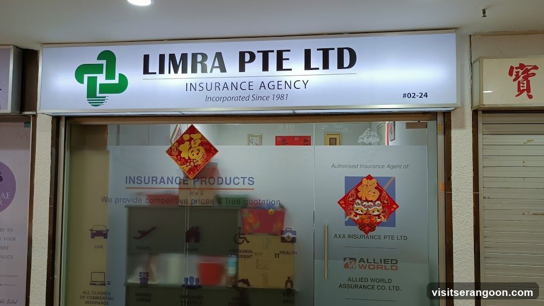 A storefront featuring a large, illuminated white sign reading 'LIMRA PTE LTD INSURANCE AGENCY' with a green logo. The unit number #02-24 is visible. The glass entrance doors display various insurance product icons (car, travel, home, health) and text stating 'We provide competitive prices & free quotation'. Red festive decorations are adhered to the glass, and logos for AXA Insurance and Allied World are visible on the right door.