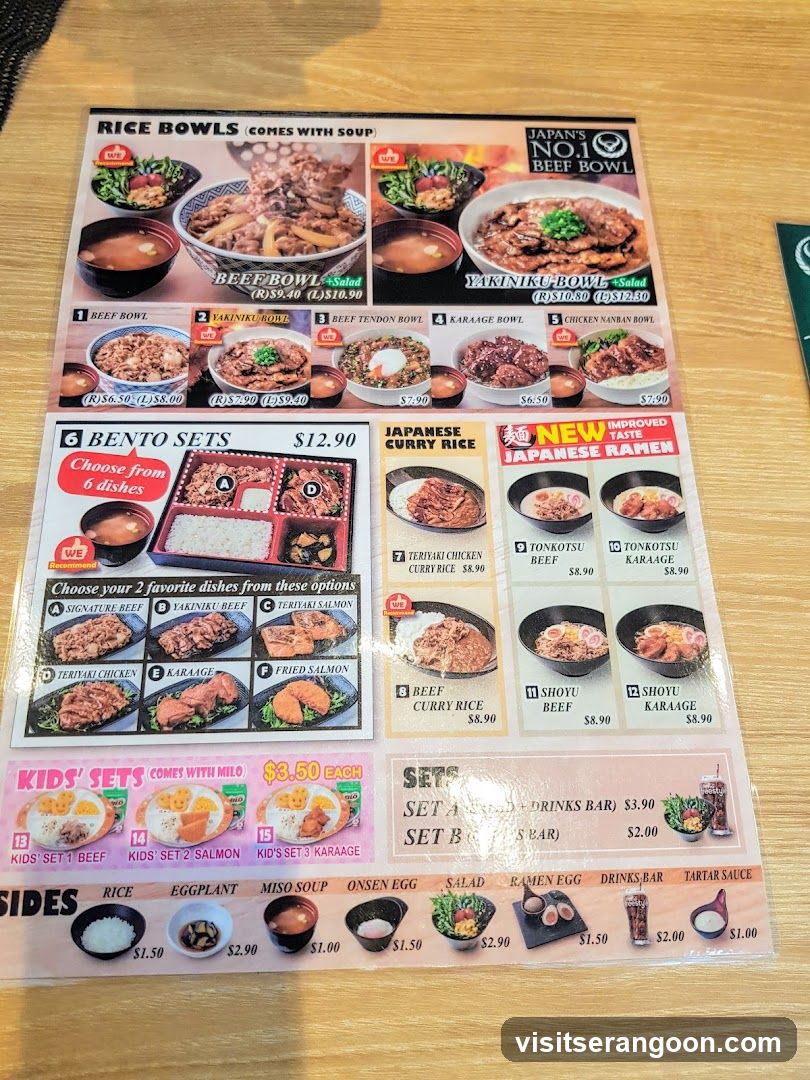 A laminated menu on a wooden table featuring sections for Rice Bowls, Bento Sets, Japanese Curry Rice, Japanese Ramen, Kids' Sets, and Sides.