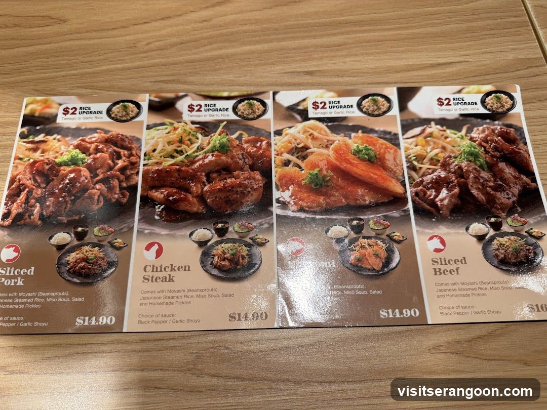 A printed menu on a wooden table showing four dishes: Sliced Pork, Chicken Steak, Salmon, and Sliced Beef. Each dish is priced at $14.90 and includes a $2 rice upgrade option.