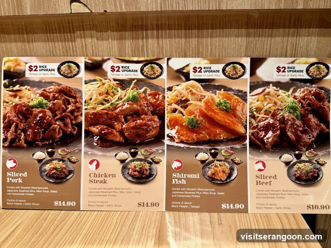 A close-up view of a four-panel menu stand on a wooden table, showcasing four different meat dishes: Sliced Pork, Chicken Steak, Shirobi Fish, and Sliced Beef. Each panel features a large photo of the dish, its name, price, and a promotional offer for a rice upgrade.