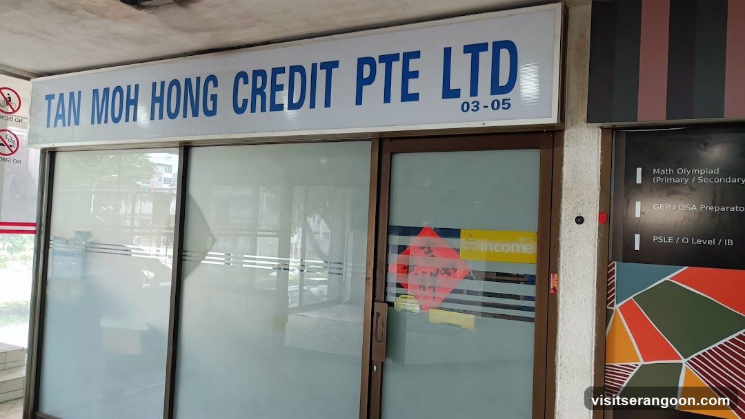 A view of a commercial storefront with a large white sign reading 'TAN MOH HONG CREDIT PTE LTD' in blue capital letters. The unit number 03-05 is visible. The entrance consists of glass doors and windows with brown frames. A red diamond-shaped sticker is on the right door, and a yellow 'income' sticker is on the glass. To the right, a black pillar displays a list of educational services including Math Olympiad, GEP/DSA Preparation, and PSLE/O Level/IB.