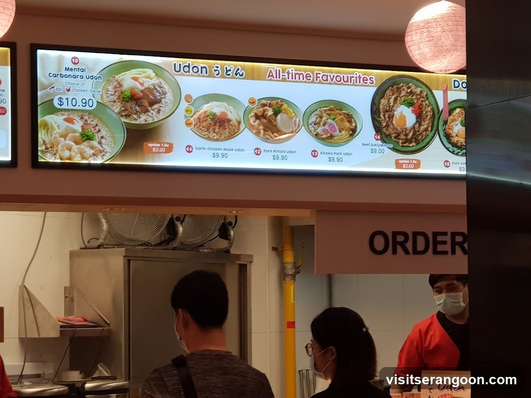 A backlit menu board displaying various udon noodle dishes with prices and images.