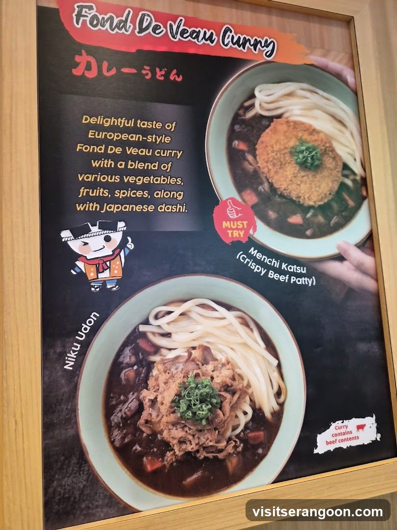 A framed menu poster advertising two types of curry udon dishes. The top dish is 'Fond De Veau Curry' featuring a crispy beef patty (Menchi Katsu), and the bottom dish is 'Niku Udon' topped with shredded meat. The poster includes descriptive text about the European-style curry and Japanese dashi blend.