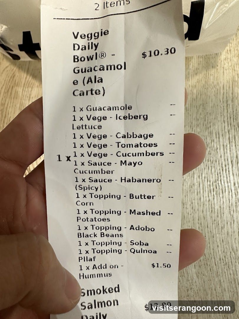 A receipt showing two items ordered. The first item is a Veggie Daily Bowl for $10.30, with a list of included ingredients and toppings. The second item is a Smoked Salmon Daily for $12.80.