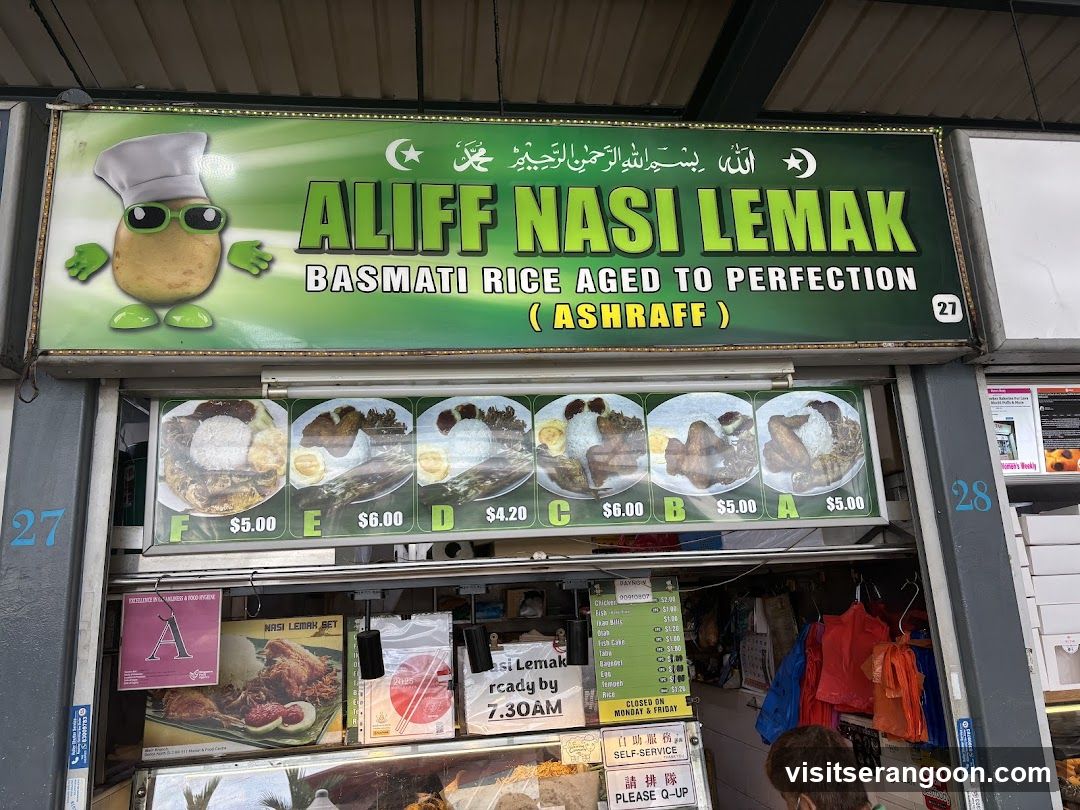 A green sign with the text "ALIFF NASI LEMAK BASMATI RICE AGED TO PERFECTION (ASHRAFF)" is displayed above a food stall. Below the sign are pictures of nasi lemak dishes with prices. The stall also displays a menu board with various food items and prices, and signs indicating self-service and operating hours.