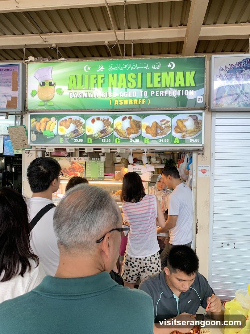 A food stall with a large green sign displaying the name "ALIFF NASI LEMAK" and images of various nasi lemak dishes. The stall is busy with customers.