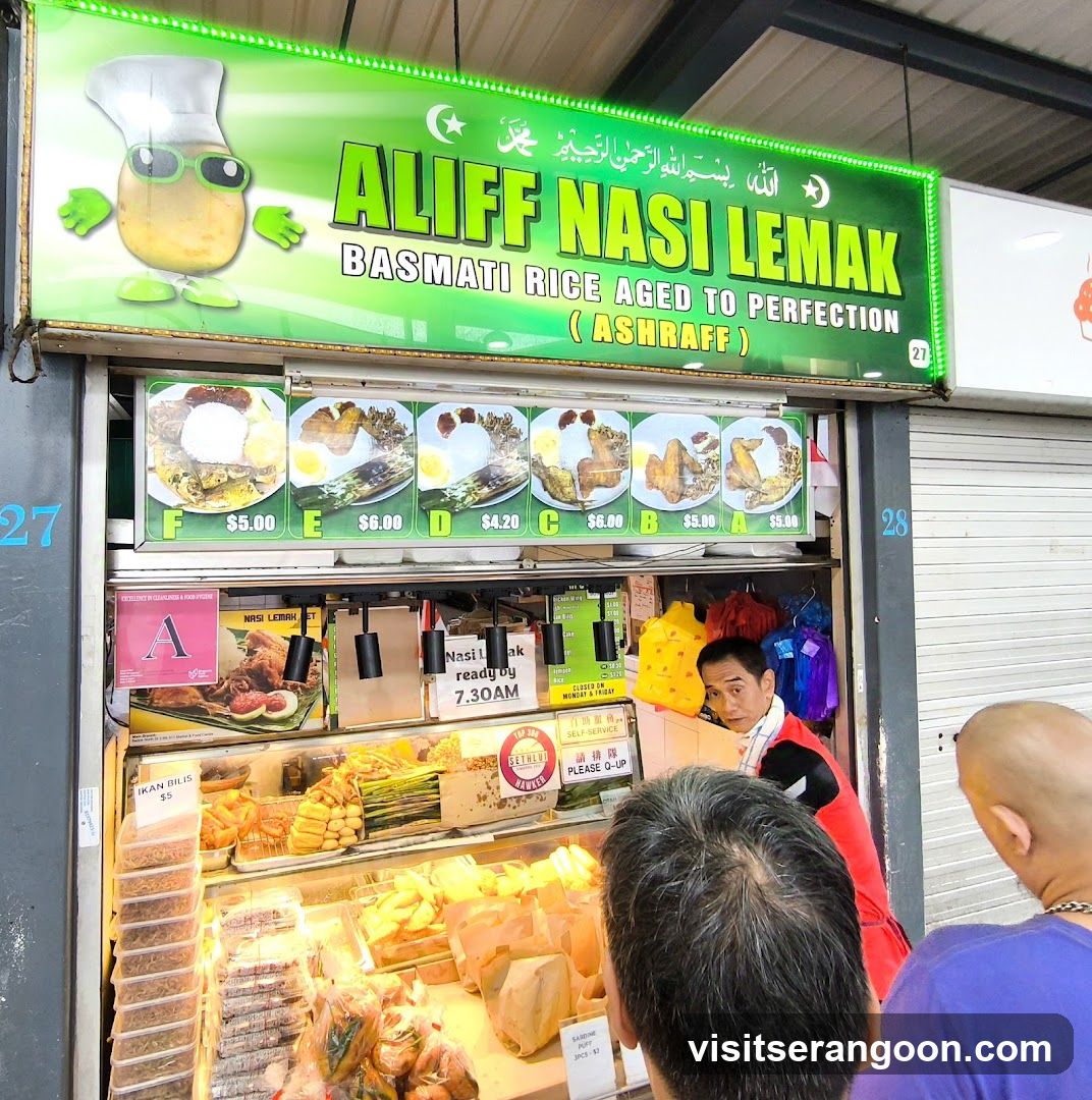 A food stall with a bright green sign that reads "ALIFF NASI LEMAK BASMATI RICE AGED TO PERFECTION (ASHRAFF)". Below the sign are pictures of different nasi lemak meals with prices ranging from $4.20 to $6.00. The stall displays various food items in refrigerated cases, including fried chicken, fish, and vegetables. A sign indicates that nasi lemak is ready by 7:30 AM and the stall is closed on Monday and Friday. There are also signs for "IKAN BILIS $5" and "SARDINE PUFF 3PCS $2". A staff member is visible behind the counter.