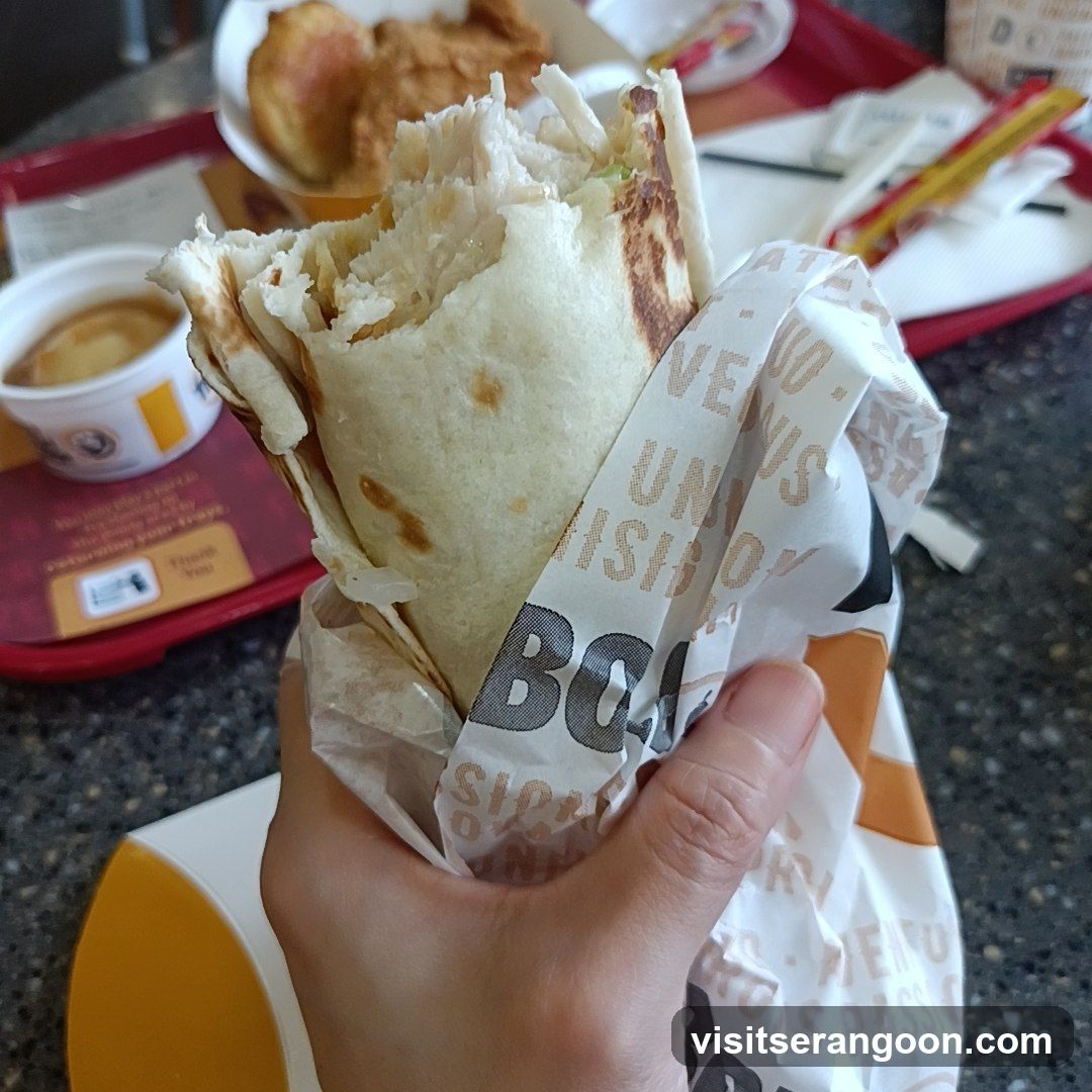 Hand holding a burrito wrapped in branded paper