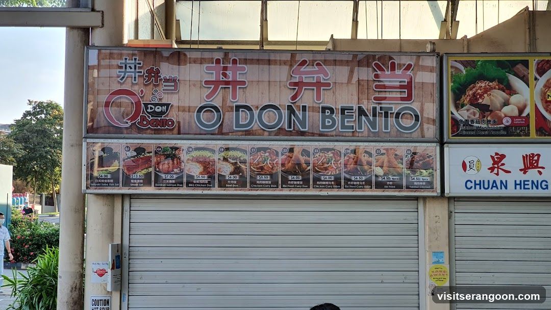 A storefront with a large sign displaying the name "O DON BENTO" in English and Chinese characters. Below the main sign, there are several smaller signs with images of food items and their prices. To the right of the O Don Bento sign, there is another sign for "CHUAN HENG". The storefront has a metal roller shutter.