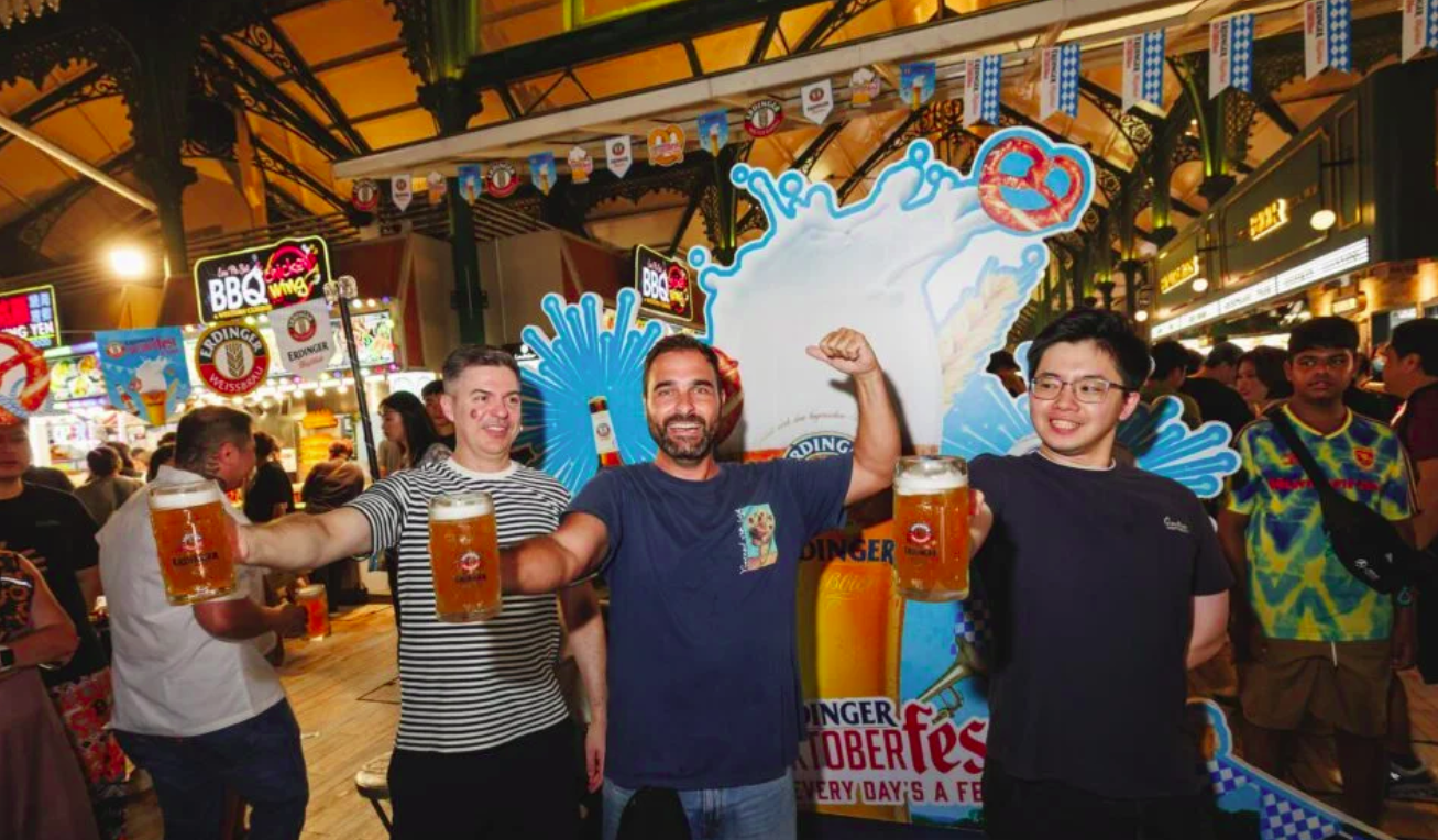 Oktoberfest crowd under festive lighting with long tables, beer steins, and a Bavarian-style beer hall setup